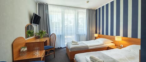 Ein Hotelzimmer mit zwei Betten, einem Schreibtisch, einem Fernseher, einem Sessel und einem Fenster mit Vorhängen.