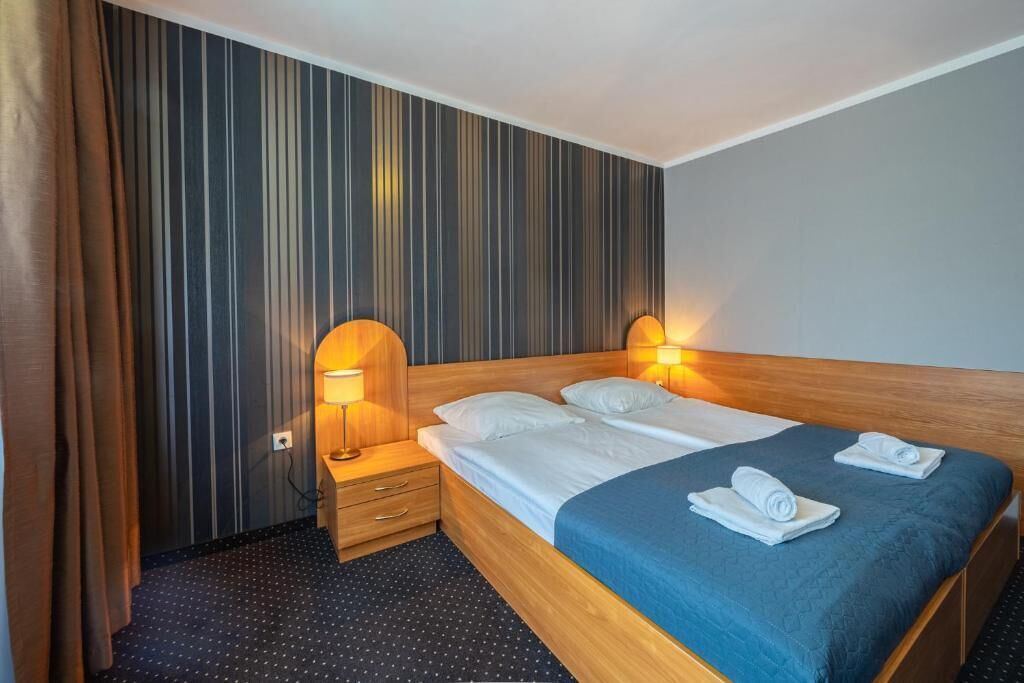 Une chambre d’hôtel avec un lit, deux lampes de chevet, une table de nuit, une couvre-lit bleue et un papier peint à rayures.