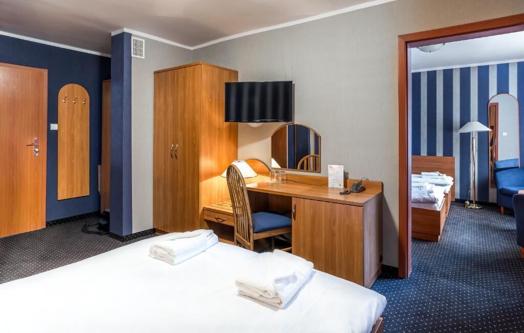 A hotel room with a bed, desk, chair, wardrobe, and a television.