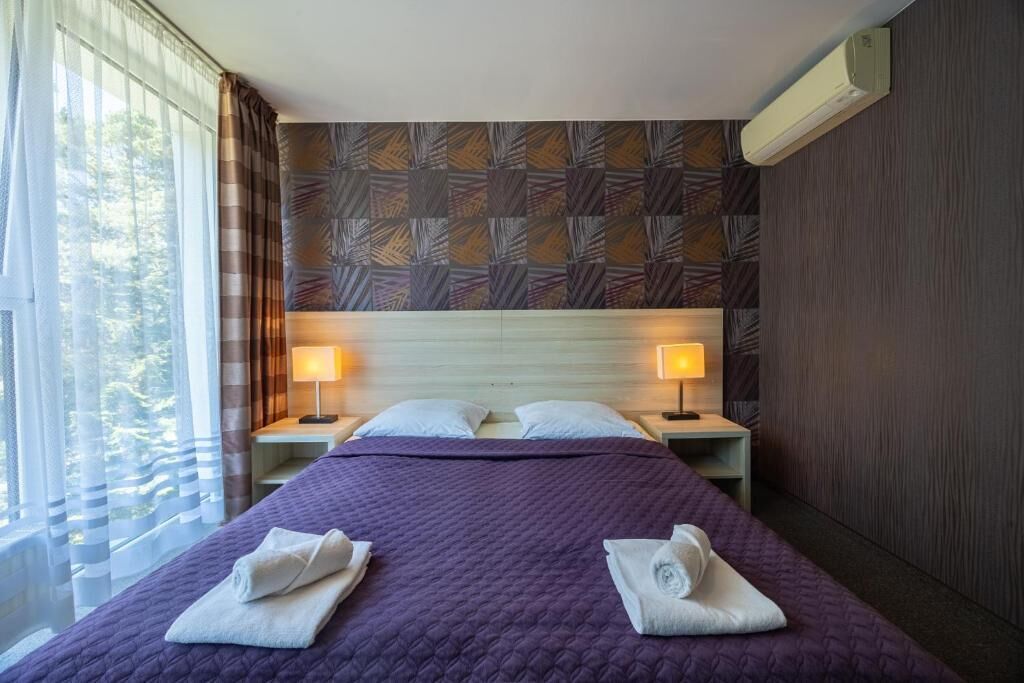 Habitació d'hotel amb un llit gran, dues taules de nit amb làmpades, una finestra amb cortines i una paret amb un disseny.