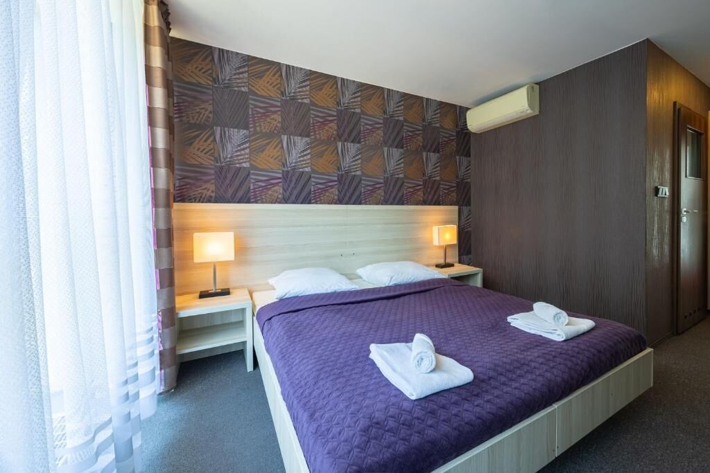 Ein Hotelzimmer mit einem Bett, zwei Nachttischen, einer Kommode, einer Wand mit einem Blattmuster und einer Tür.