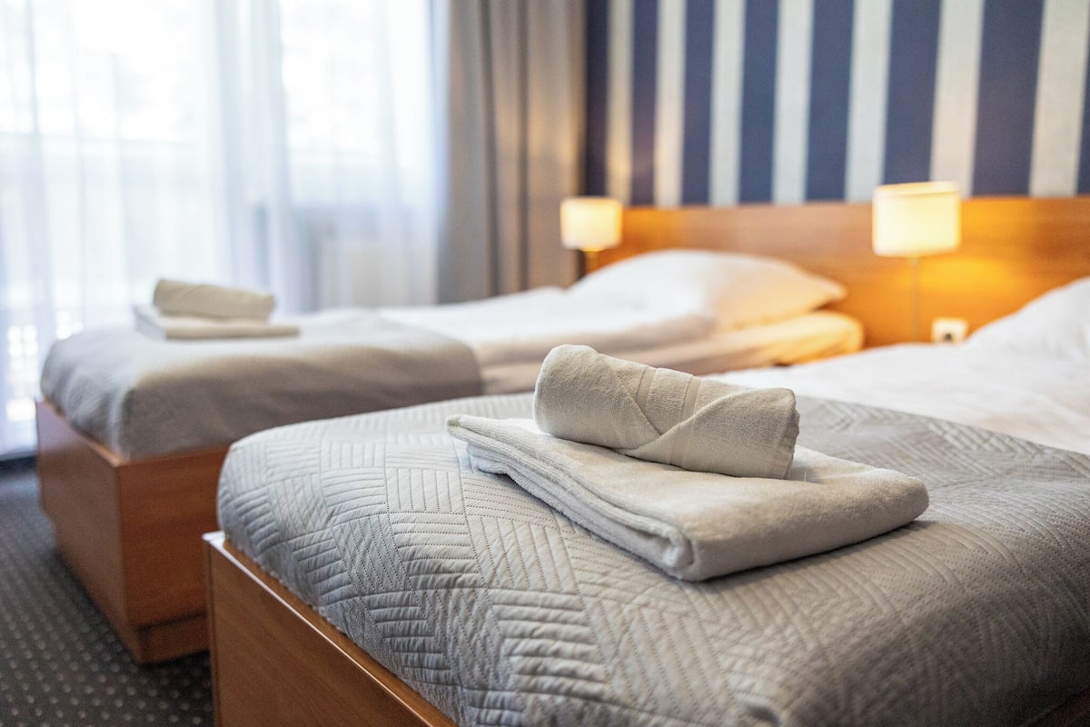 Two neatly made beds with folded towels, a wooden headboard, and a striped wall in the background.