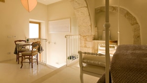 A room with a stone wall, a bed, a chair, a table with chairs, and a hanging light fixture. - Sotto Le Stelle (Picinisco)