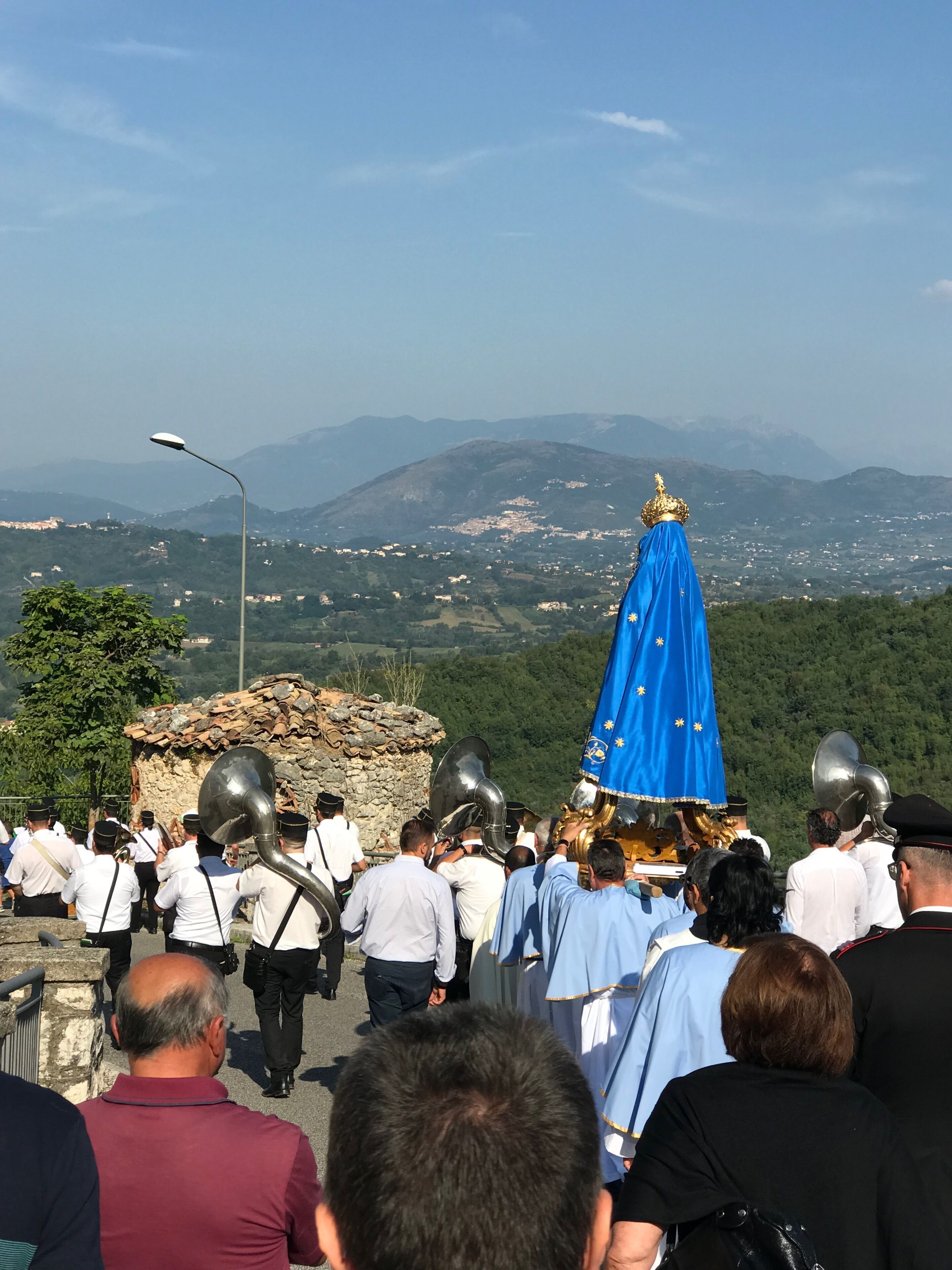 A group of people in white shirts and black hats walking towards a statue with a blue cloth and a golden crown.