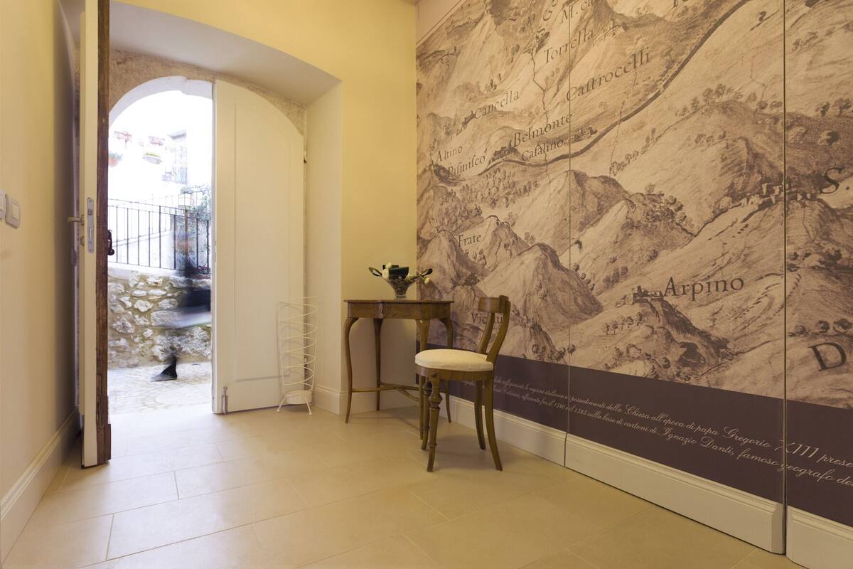 A hallway with a marble wall featuring a map, a wooden chair, and a small table with a vase.