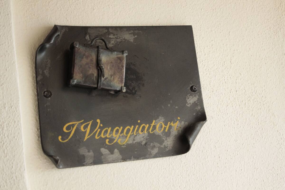 A black metal plaque with the inscription "I Viaggiatori" mounted on a wall.