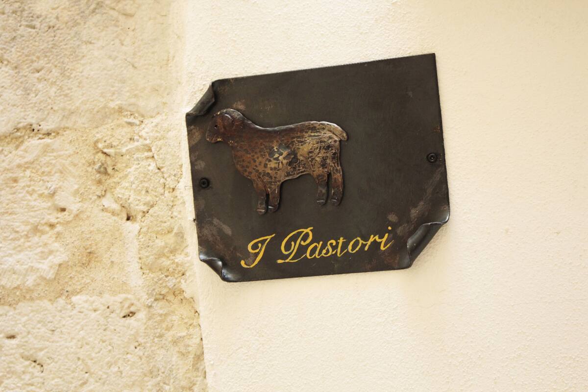 A metal plaque with a sheep and the inscription "I Pastori" mounted on a wall.
