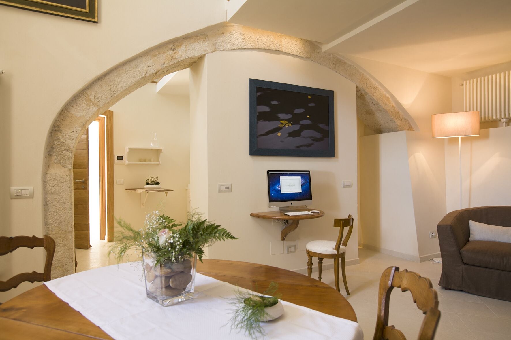 Un coin repas agrémenté d’une arche en pierre, un ordinateur posé sur une petite table et une lampe.