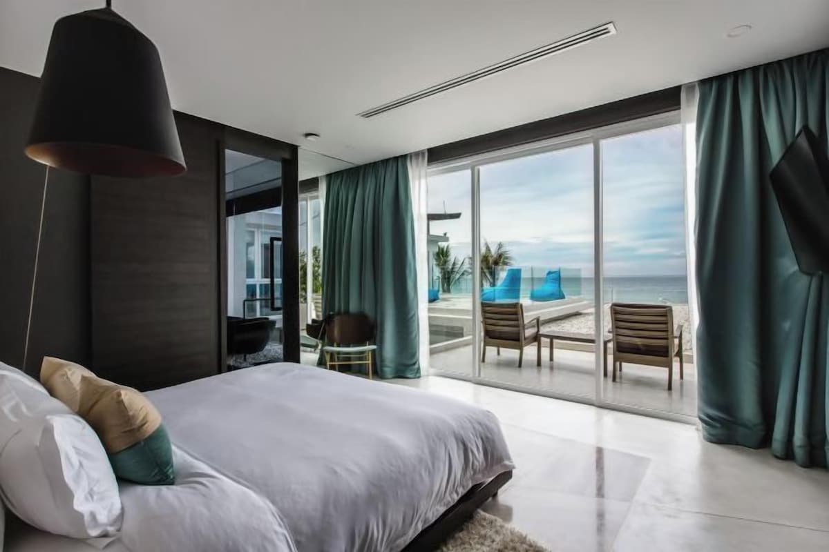 Ein modernes Schlafzimmer mit einem großen Bett, Blick auf den Strand und einem Balkon mit Sitzgelegenheit.