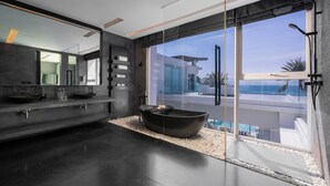 A modern bathroom with a large bathtub, a double sink, and a large window offering a view of the pool and ocean. - Coastal Escape Natai Beach (Takua Thung)
