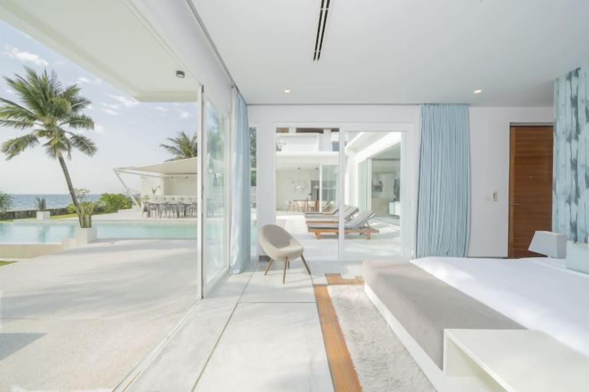 Ein modernes Hotelzimmer mit einer großen Glasdoor, die auf einen Balkon mit Pool, Sitzgelegenheit und Meerblick führt.