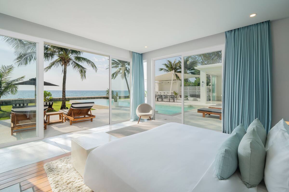 Ein Schlafzimmer mit großem Bett, Meerblick, Poolbereich und Essbereich mit Außenbestuhlung.