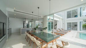 A modern kitchen with a central island, bar seating, and a poolside area with lounge chairs. - Coastal Escape Natai Beach (Takua Thung)