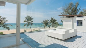 A modern balcony with a white sofa, a glass door, and a view of the beach and ocean. - Coastal Escape Natai Beach (Takua Thung)