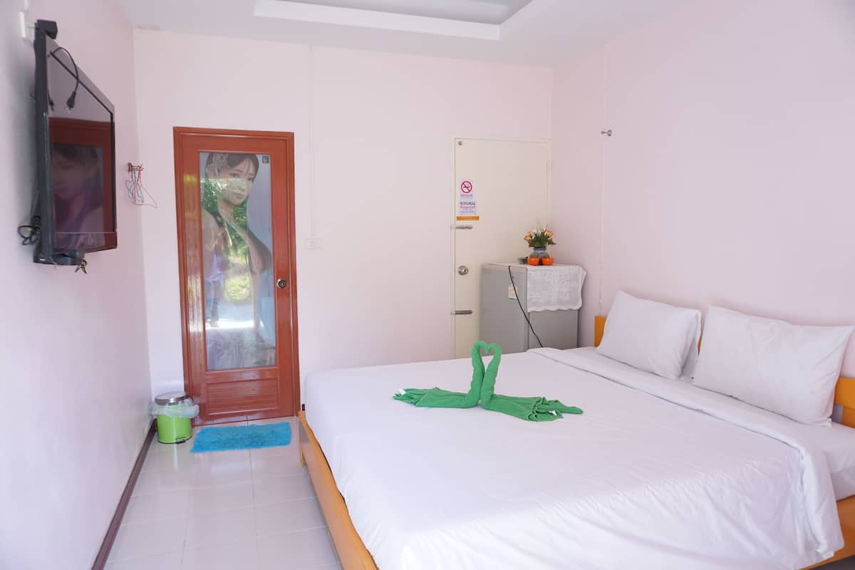 A hotel room with a bed, a door, a mirror, a small table with a plant, and a trash bin.