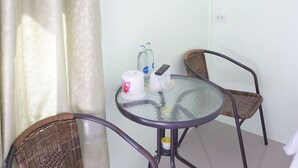 A room with a glass table, two wicker chairs, a curtain, an air conditioning unit, and a bottle of water. - Go Green Resort (Chumphon)