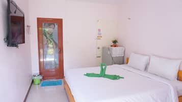 A hotel room with a bed, a door, a mirror, a small table with a plant, and a trash bin.