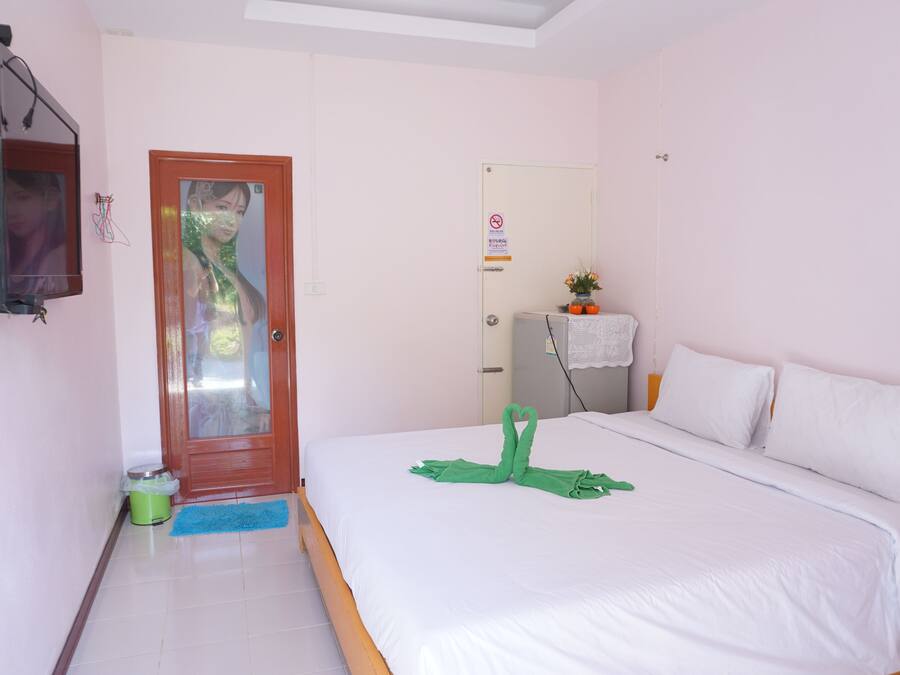 A hotel room with a bed, a door, a mirror, a small table with a plant, and a trash bin.