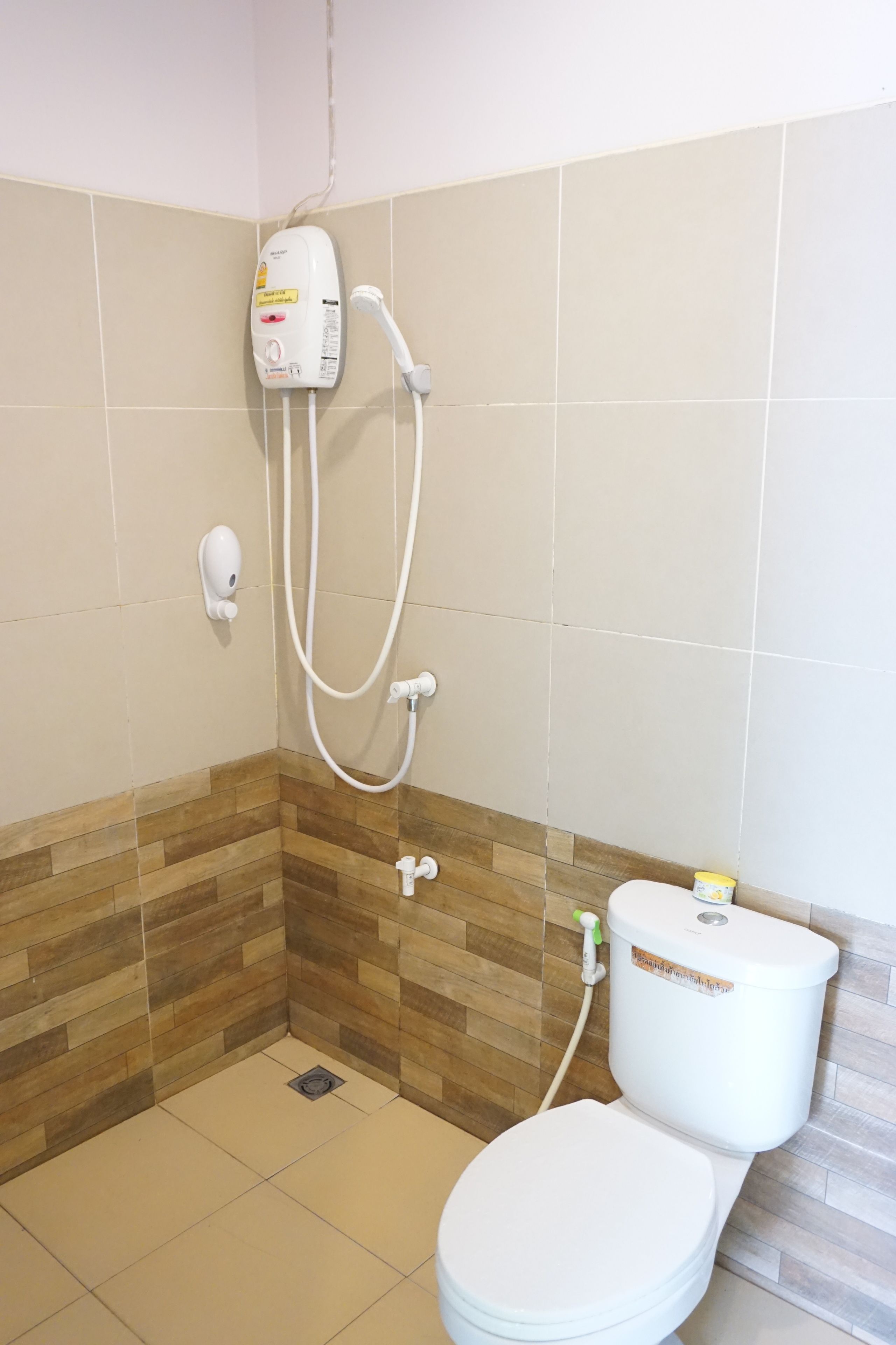 A bathroom with a shower, toilet, and a soap dispenser.