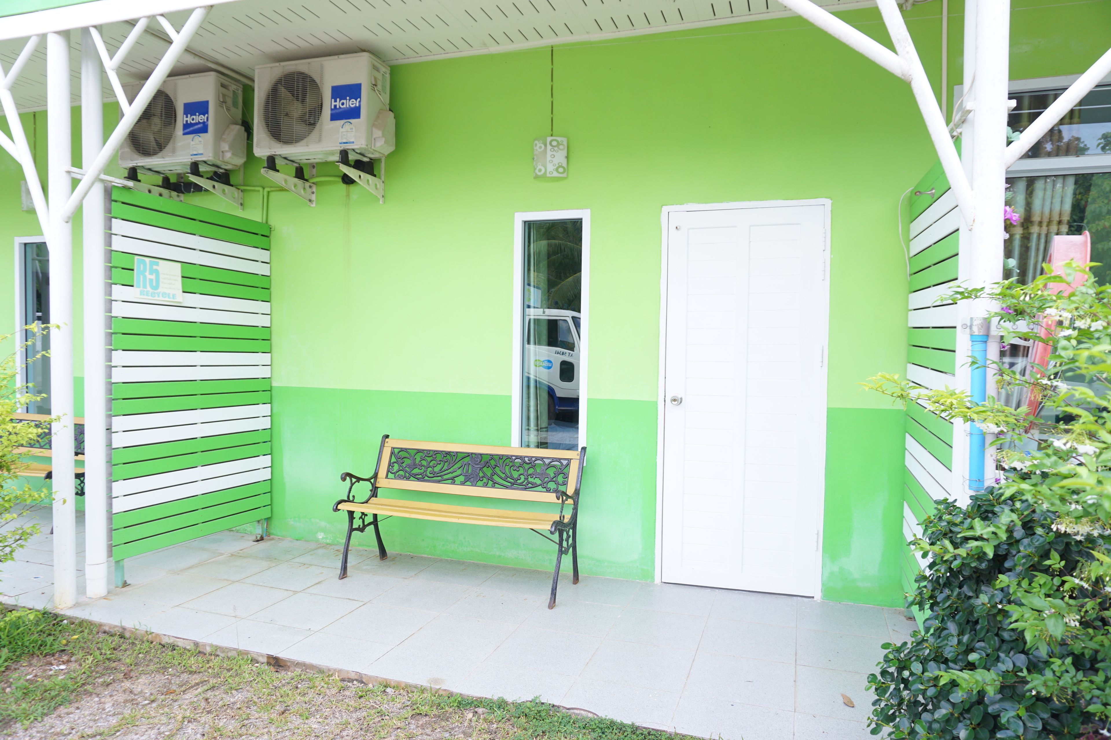 Un bâtiment vert avec un banc à l’extérieur, une porte et deux unités de climatisation.