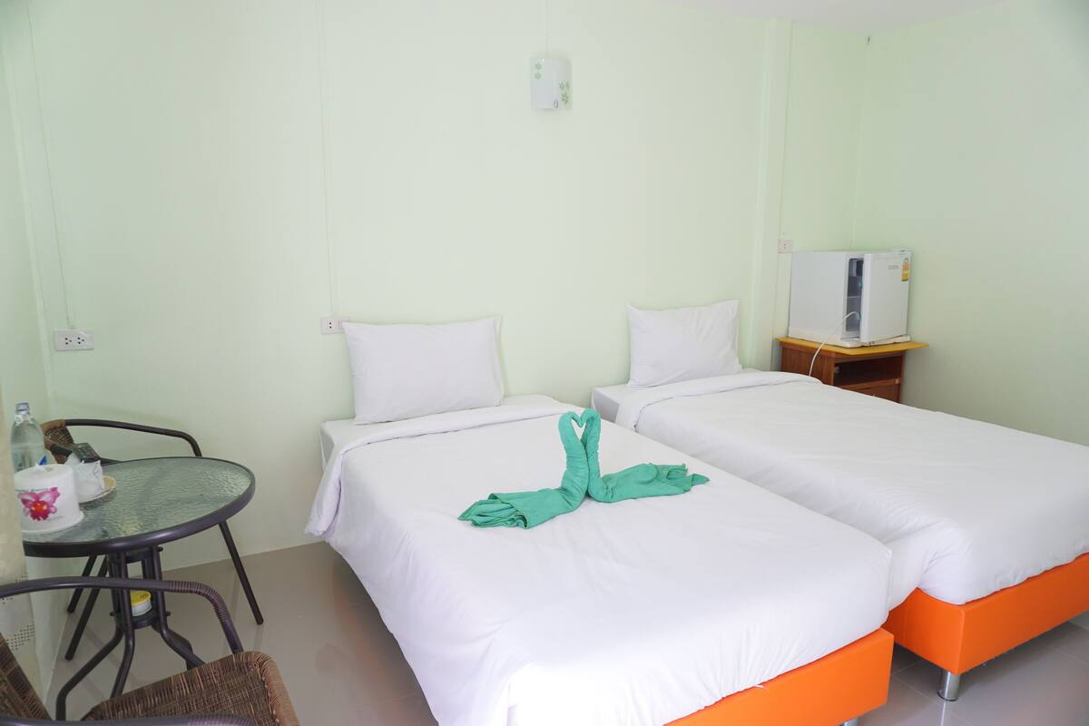 A hotel room with two beds, a small table with a bottle and a cup, and a chair.