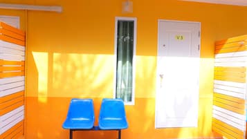 A corridor with two blue chairs, a white door labeled "V3", and a window with a curtain.