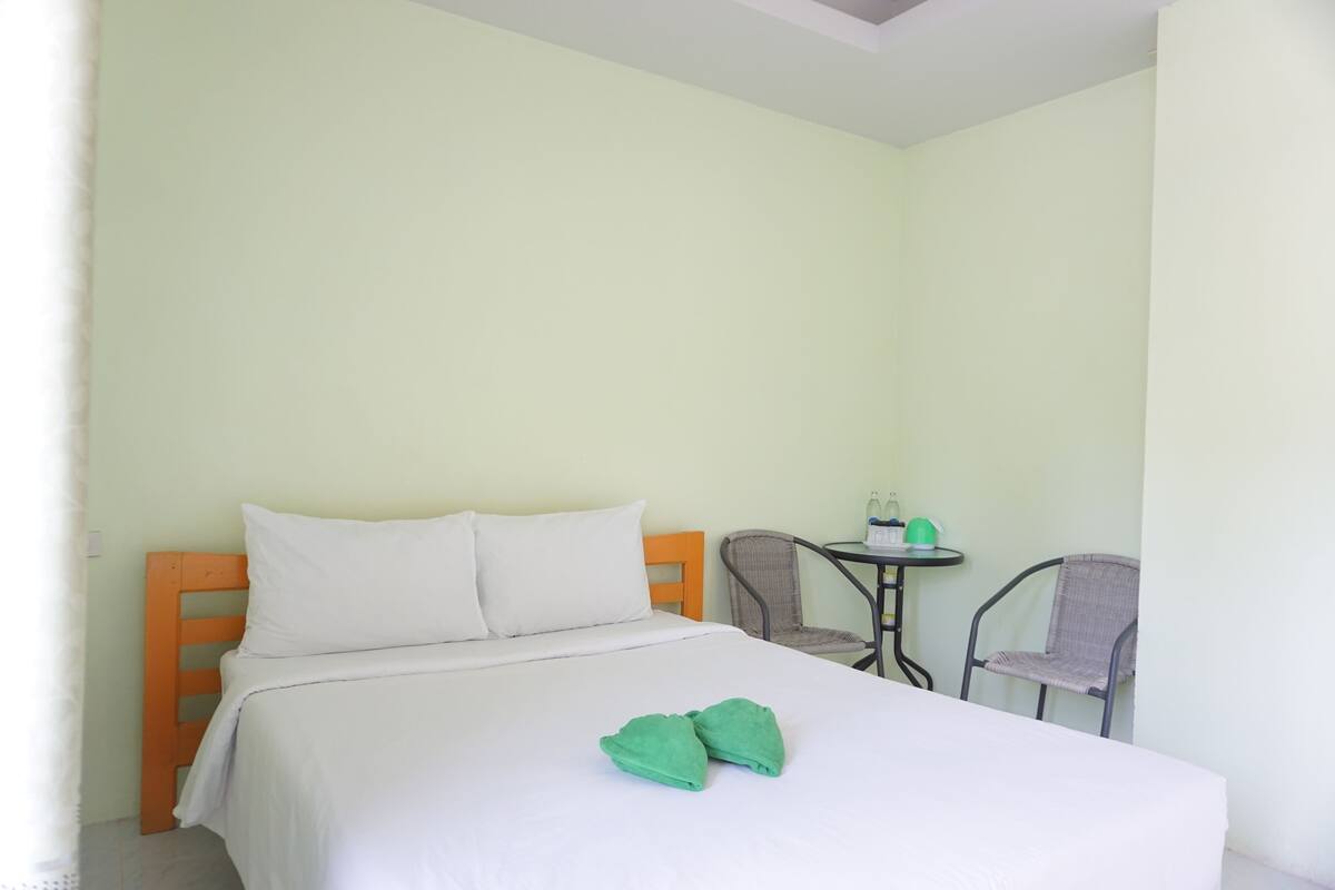 A neatly made bed with white bedding and two green towels placed on it.