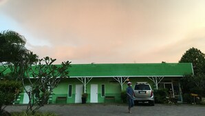 A green building with a white door and windows, a bench, and a car parked in front. - Go Green Resort (Chumphon)