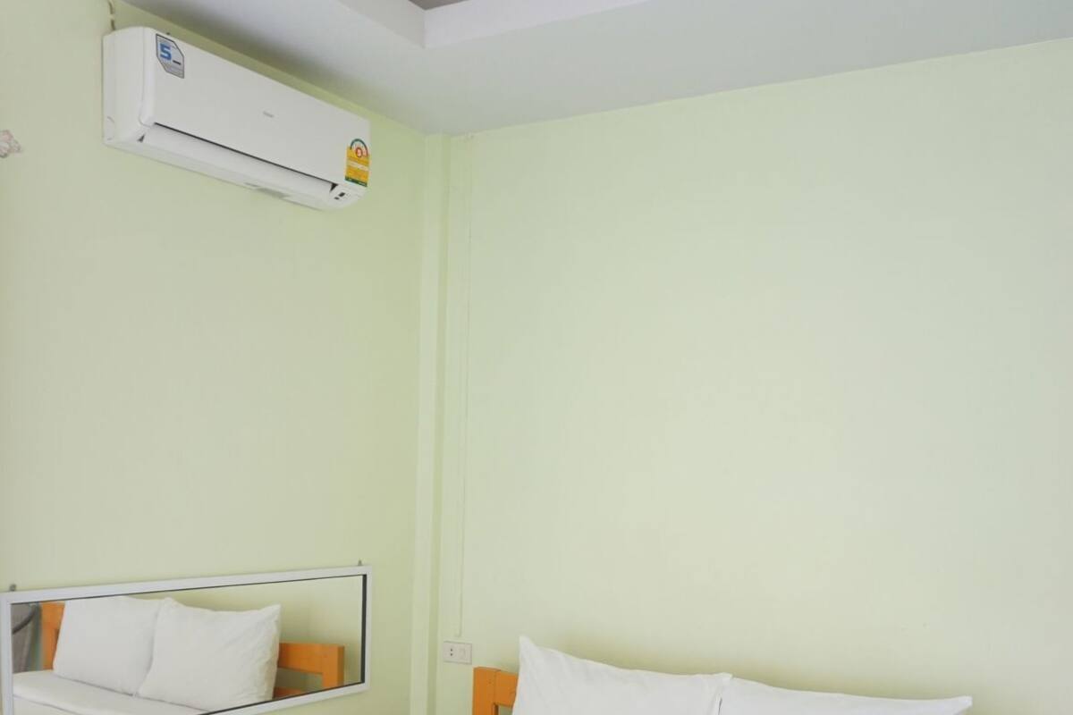 A hotel room with a bed, a mirror, an air conditioning unit, and a green pillow.