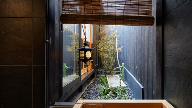 Um quarto japonês tradicional com tatames, uma porta de correr de madeira e vista para um jardim através de uma janela.