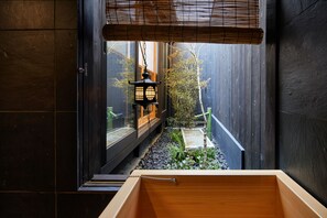 A traditional Japanese room with tatami flooring, a wooden sliding door, and a view of a garden through a window. - Kyoto Urushiro Wakasaya (Kyoto)