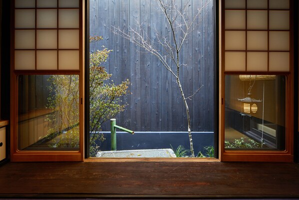 A traditional Japanese room with tatami flooring, a wooden sliding door, and a view of a garden with a tree and a small pond. - Kyoto Urushiro Wakasaya (Kyoto)