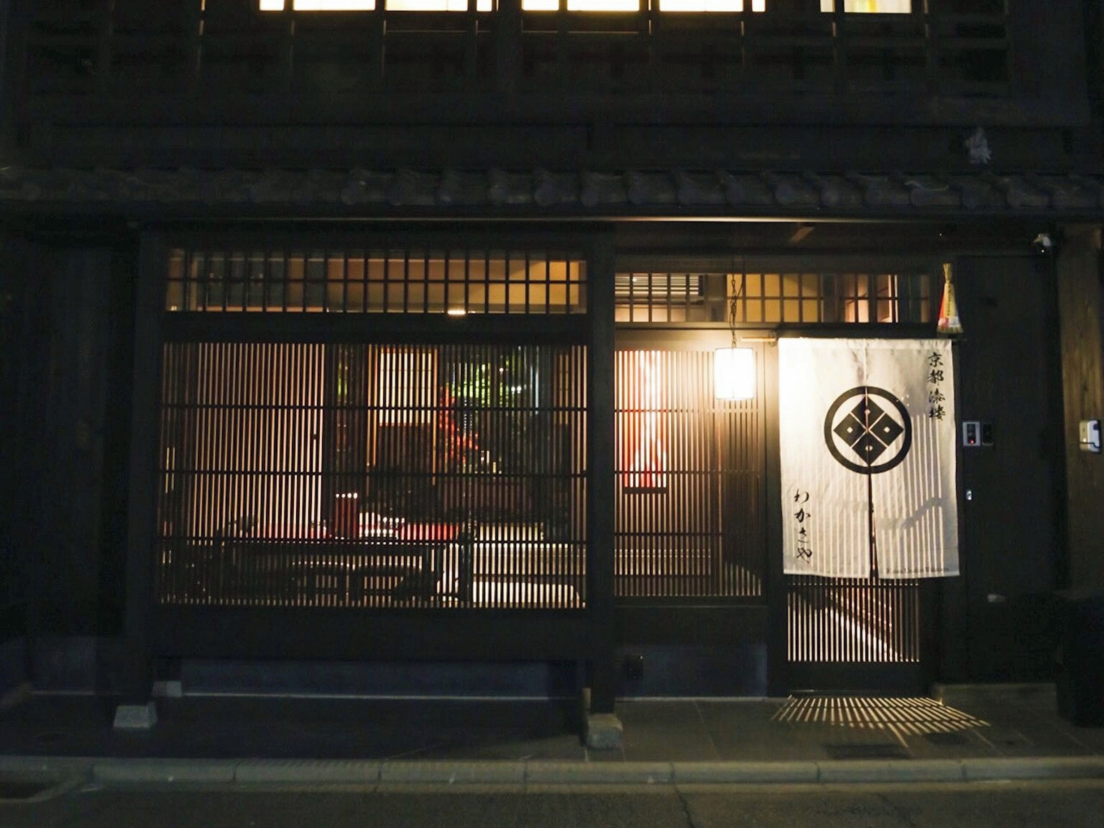 A traditional Japanese building with a wooden exterior, a black gate with vertical slats, and a sign with Japanese characters.