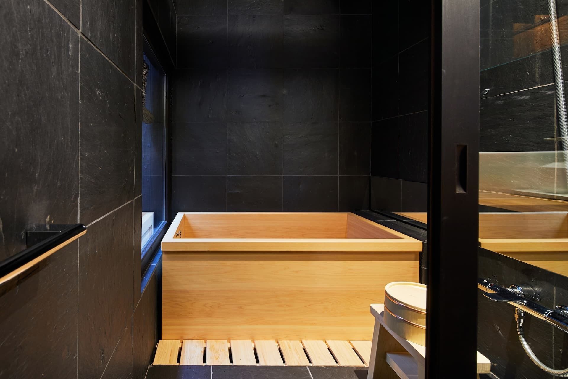 Un baño moderno con una bañera de madera, inodoro y cabina de ducha de cristal.