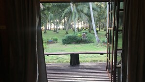 A room with a bed, a view of a garden with palm trees, and a wooden deck.