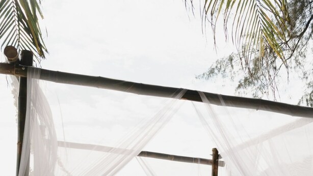 A beach wedding setup with a white canopy and floral decorations.