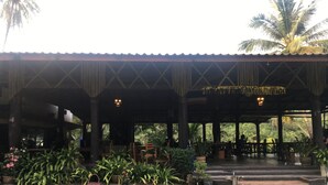 An outdoor covered area with wooden pillars, potted plants, and a seating arrangement.