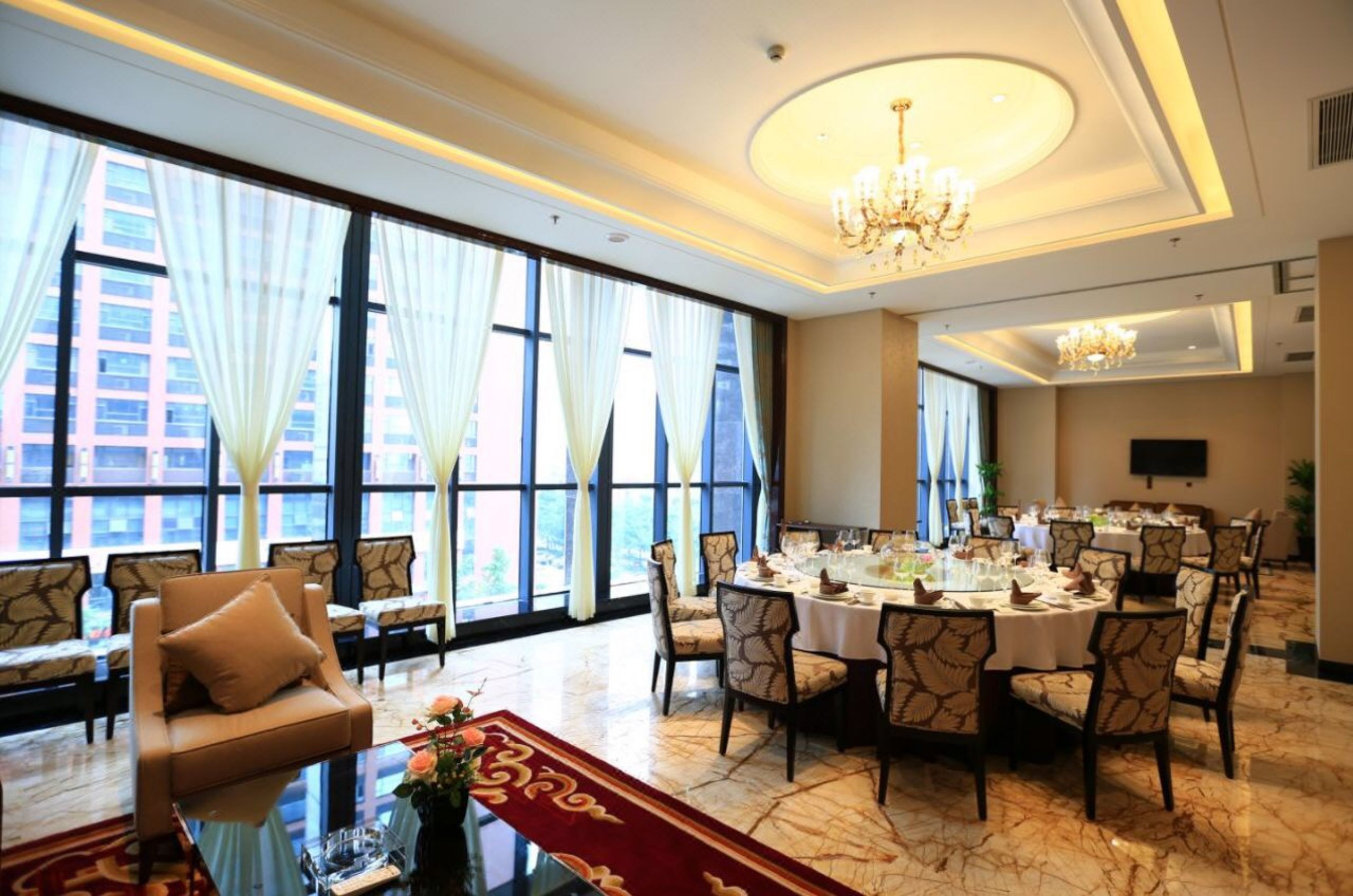 A hotel dining area with a large round table set for a meal, surrounded by upholstered chairs.