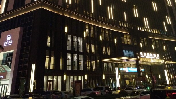 A multi-story hotel with illuminated vertical lines on the facade, large windows, and a parking lot with several cars. - Lanxi International Hotel  (Xi'an)