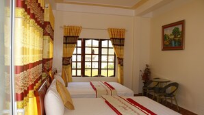 Camera d'albergo con due letti, una finestra con tende, un tavolino con sedie e un quadro appeso al muro.
