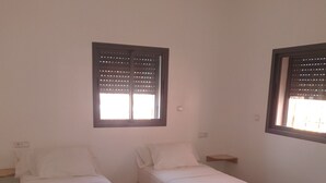 Two single beds with wooden frames and white bedding, a small red rug, and a window with blinds.
