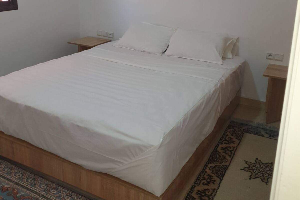 Ein schlichter, sauberer Raum mit einem Bett, Nachttischen und einem gemusterten Teppich.