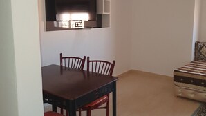 A compact living space with a dining table and chairs, a kitchenette, and a patterned sofa.