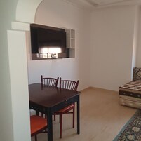 A compact living space with a dining table and chairs, a kitchenette, and a patterned sofa.