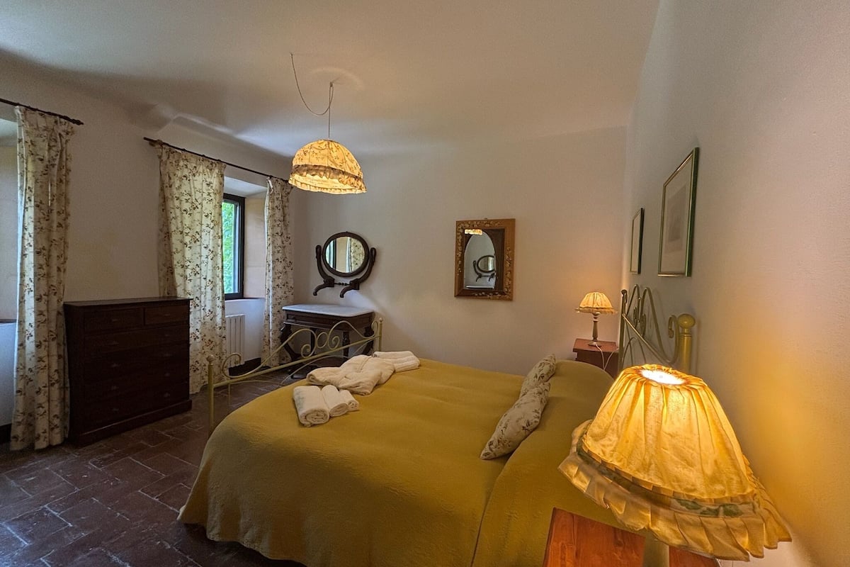 A bedroom with a bed, a dresser, a vanity with a mirror, and a lamp.
