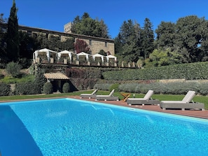 A swimming pool with lounge chairs, a stone building with a terrace, and a forested hillside. - Castello di Santa Cristina (Grotte di Castro)