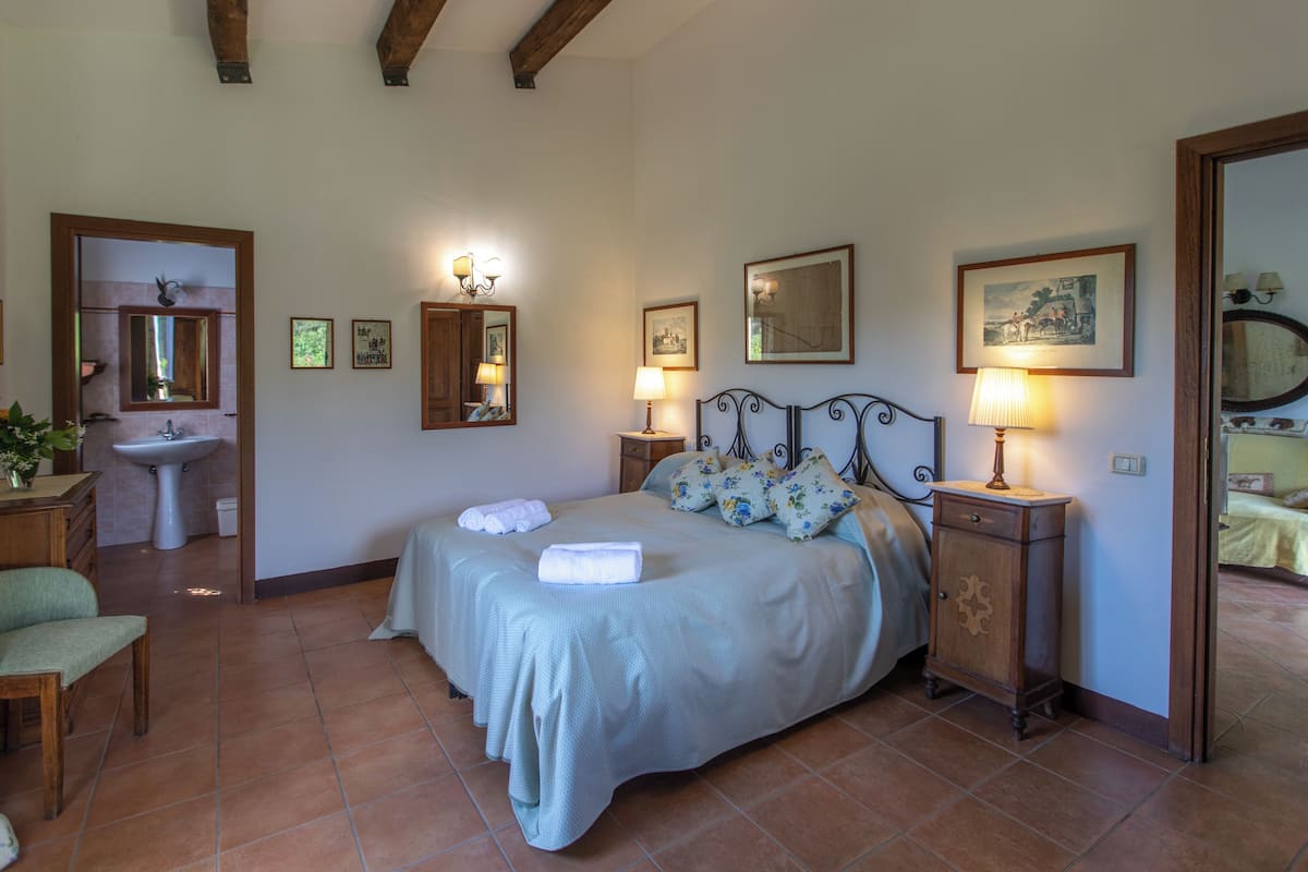 A bedroom with a bed, bedside tables, a mirror, a sink, and a chair.