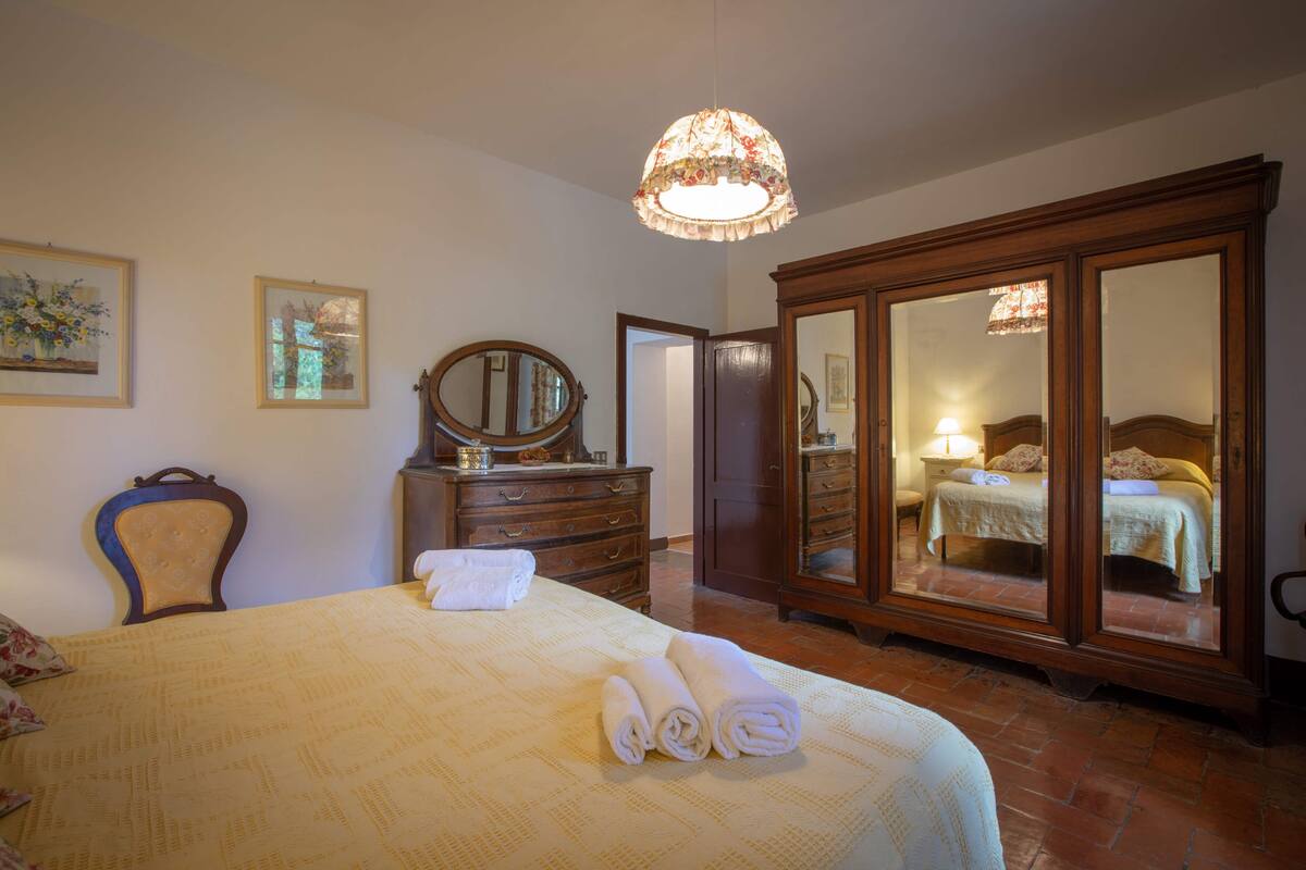 A bedroom with a large bed, a dresser, a mirror, and a wardrobe.