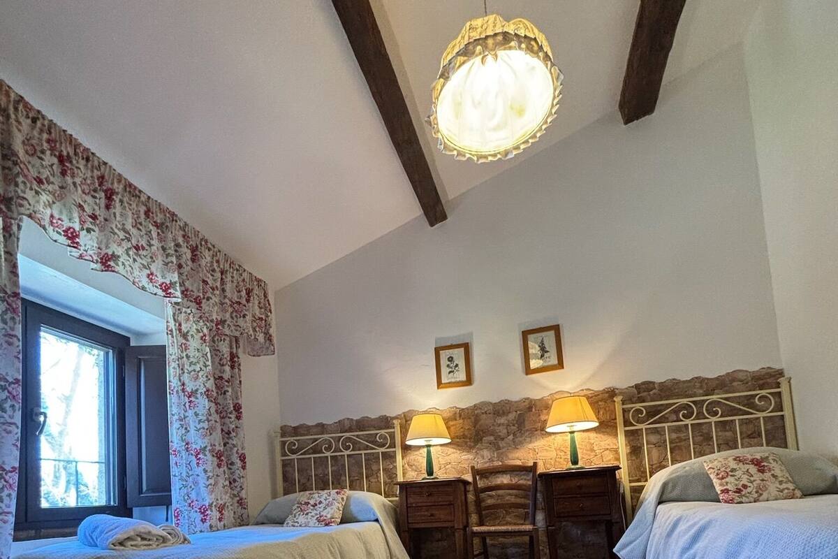 A cozy room with two beds, a wooden table, and a stone wall.