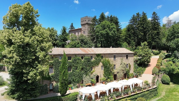 A stone building with a tiled roof, surrounded by lush greenery and a tower. - Castello di Santa Cristina (Grotte di Castro)